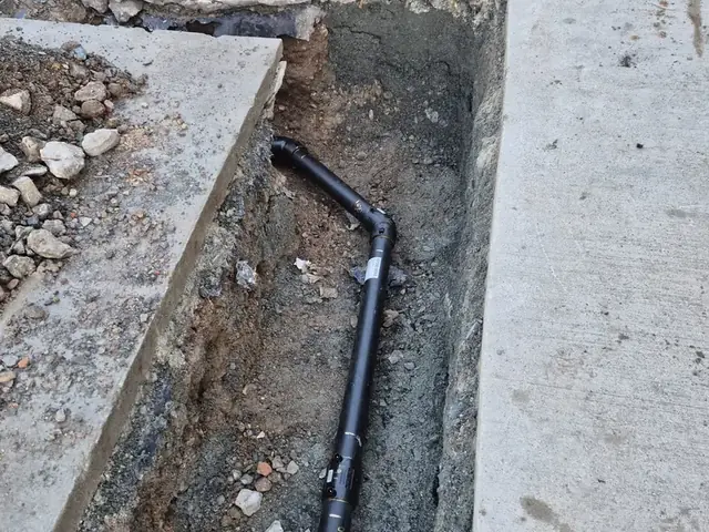 New pipe run laid in a narrow trench cut through a concrete drive