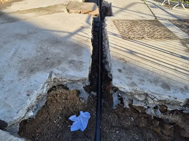 New pipe run laid in a narrow trench cut through concrete paving