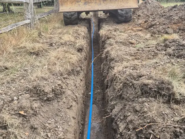 New blue MDPE supply pipe laid in a narrow trench across a field