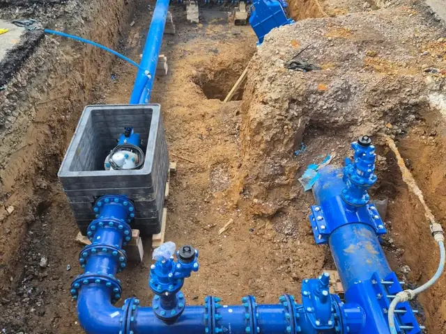 New water main, valve assembly and meter chamber in a road excavation