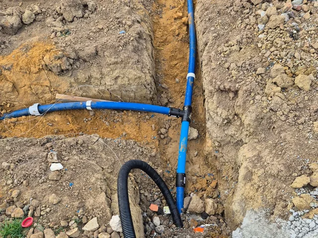 Blue water service tee and black ducting run together in an open trench